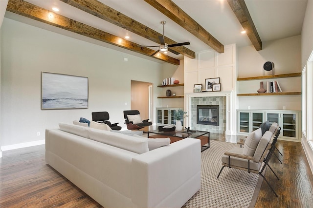 living room with ceiling fan, dark hardwood / wood-style flooring, a tiled fireplace, and beam ceiling