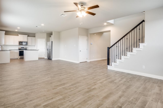 unfurnished living room with sink, ceiling fan, and light wood-type flooring