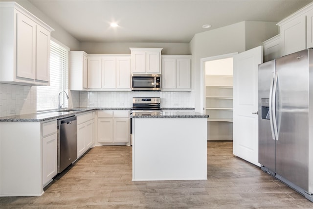 kitchen with sink, a center island, dark stone countertops, stainless steel appliances, and white cabinets