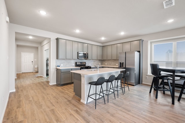 kitchen featuring gray cabinets, a kitchen island with sink, a breakfast bar, and appliances with stainless steel finishes