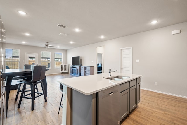 kitchen featuring a breakfast bar, sink, light wood-type flooring, stainless steel dishwasher, and an island with sink