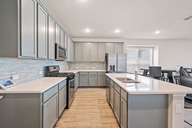 kitchen featuring gray cabinets, sink, an island with sink, and stainless steel appliances