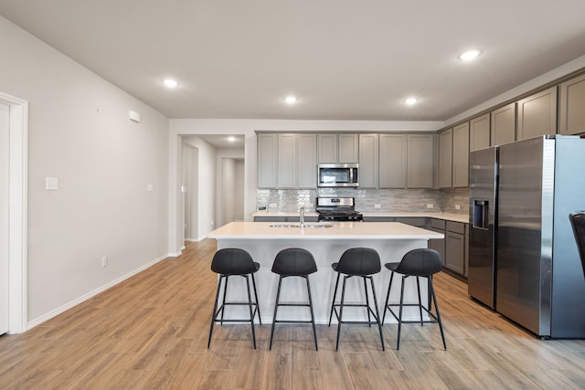 kitchen with sink, a kitchen bar, decorative backsplash, stainless steel appliances, and a center island with sink