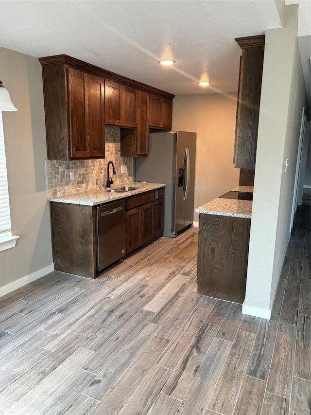 kitchen with light stone countertops, dark brown cabinetry, appliances with stainless steel finishes, light hardwood / wood-style floors, and sink