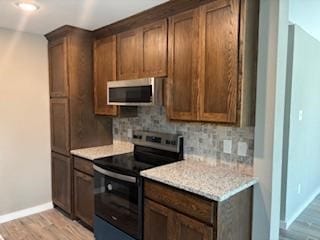 kitchen featuring light hardwood / wood-style floors, light stone countertops, stainless steel appliances, and tasteful backsplash