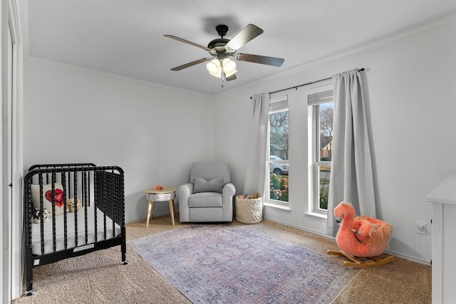 bedroom with a crib, ornamental molding, carpet, and ceiling fan