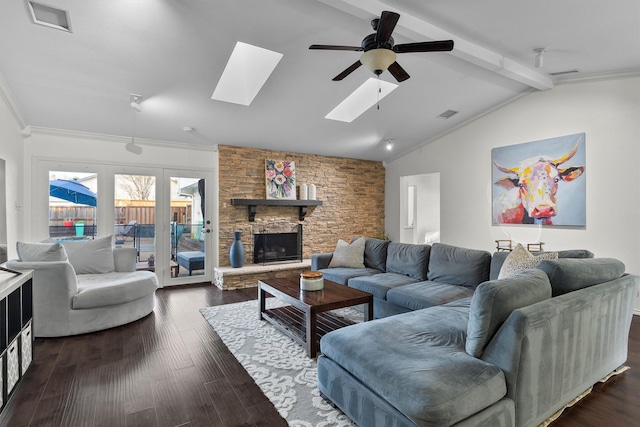 living room with a stone fireplace, dark hardwood / wood-style floors, vaulted ceiling with skylight, ornamental molding, and ceiling fan