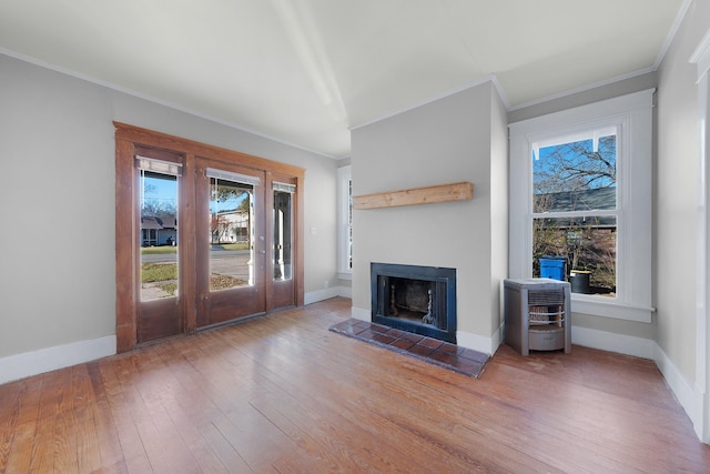 unfurnished living room featuring hardwood / wood-style floors, heating unit, ornamental molding, and a tiled fireplace