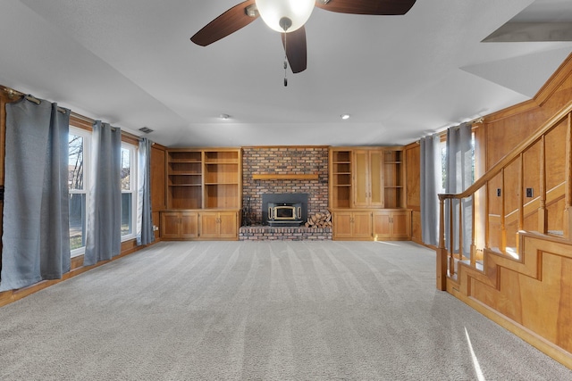 unfurnished living room with a wood stove, a wealth of natural light, built in features, and light carpet