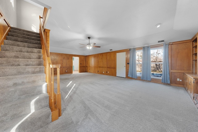 unfurnished living room featuring ceiling fan, wood walls, and light colored carpet