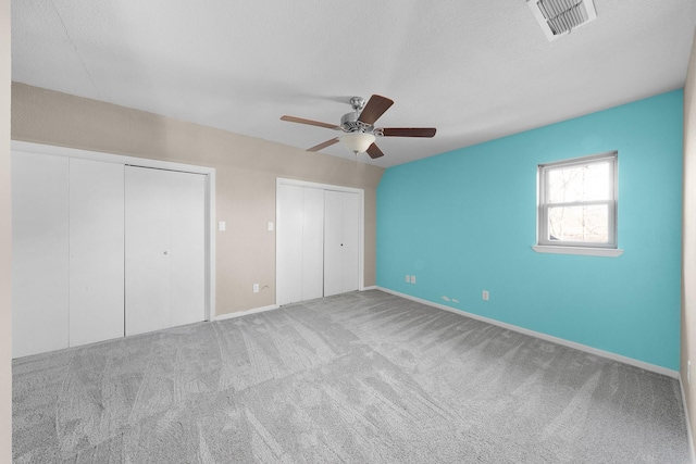 unfurnished bedroom with ceiling fan, carpet floors, a textured ceiling, and two closets