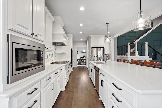 kitchen with stainless steel appliances, a center island with sink, pendant lighting, and white cabinets