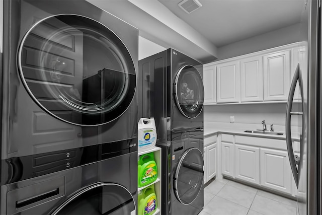 clothes washing area featuring stacked washer / drying machine, light tile patterned floors, cabinets, and sink