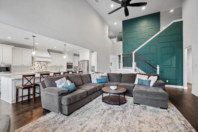 living room featuring dark wood-type flooring, ceiling fan, and a towering ceiling