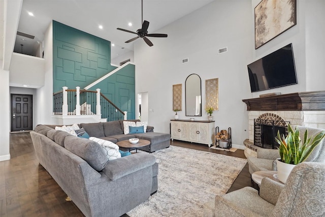 living room featuring dark wood-type flooring, a fireplace, ceiling fan, and a high ceiling