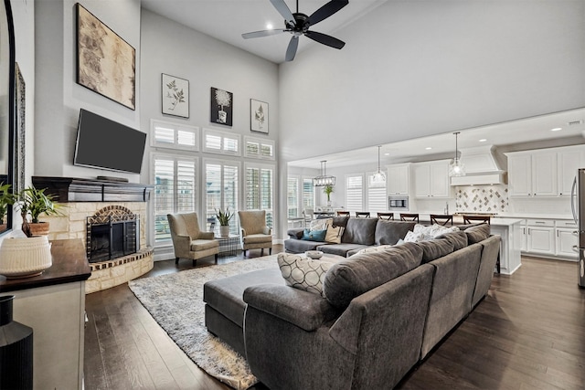 living room with a healthy amount of sunlight, a stone fireplace, dark wood-type flooring, and ceiling fan