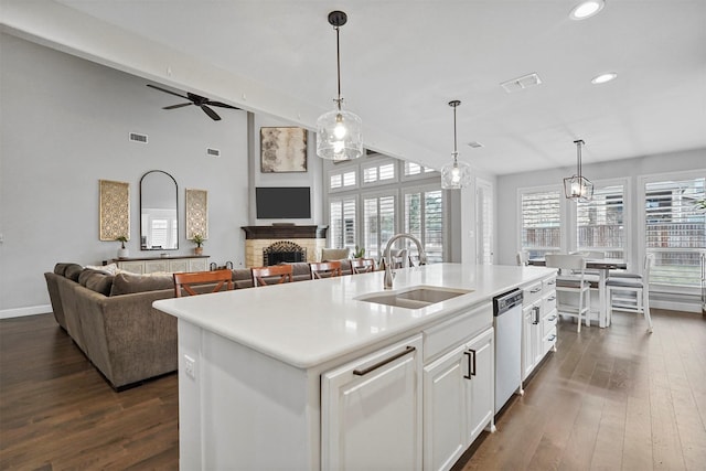 kitchen with sink, a center island with sink, stainless steel dishwasher, pendant lighting, and a fireplace