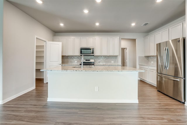 kitchen featuring light stone countertops, white cabinetry, a kitchen island with sink, appliances with stainless steel finishes, and light wood-type flooring