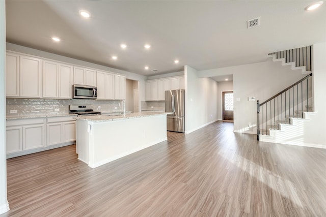 kitchen featuring white cabinets, light stone countertops, light wood-type flooring, an island with sink, and stainless steel appliances