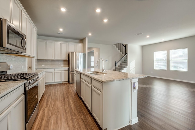 kitchen featuring white cabinets, sink, an island with sink, appliances with stainless steel finishes, and wood-type flooring