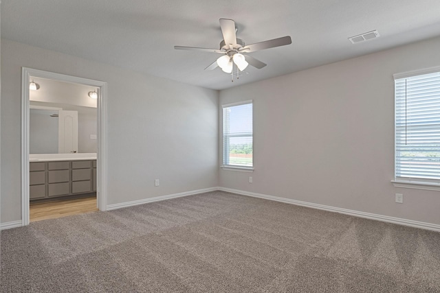 unfurnished bedroom with multiple windows, connected bathroom, light carpet, and ceiling fan