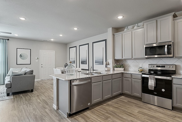 kitchen featuring sink, kitchen peninsula, gray cabinets, appliances with stainless steel finishes, and light wood-type flooring