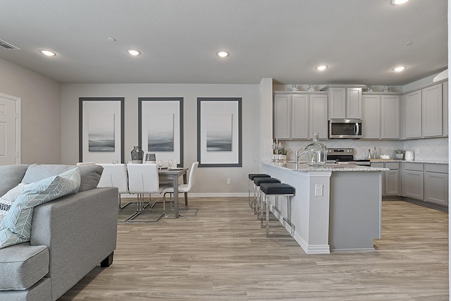 kitchen with gray cabinets, light hardwood / wood-style floors, light stone countertops, and stainless steel appliances