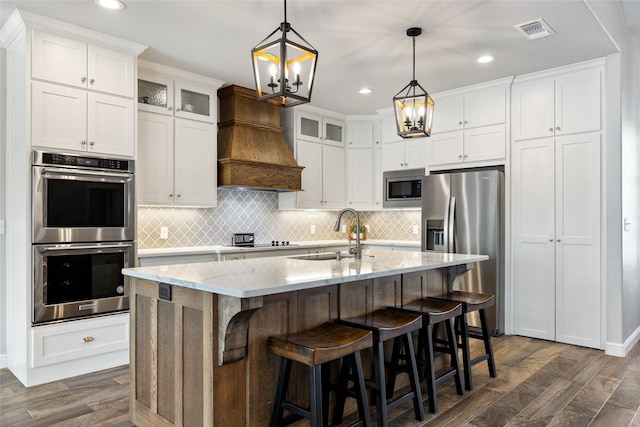 kitchen featuring sink, appliances with stainless steel finishes, an island with sink, white cabinets, and custom exhaust hood