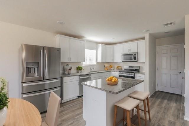 kitchen with stainless steel appliances, light stone countertops, white cabinets, a kitchen island, and dark hardwood / wood-style flooring