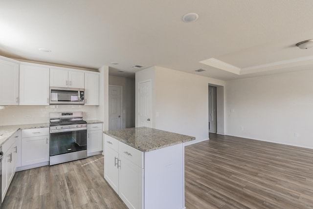 kitchen with stainless steel appliances, a center island, white cabinets, and a tray ceiling