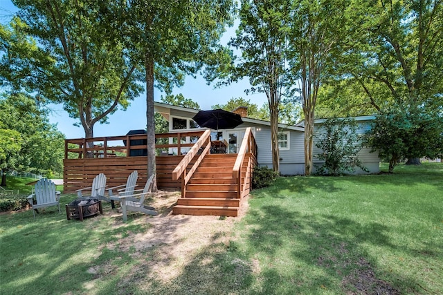 rear view of house featuring a wooden deck, an outdoor fire pit, and a lawn