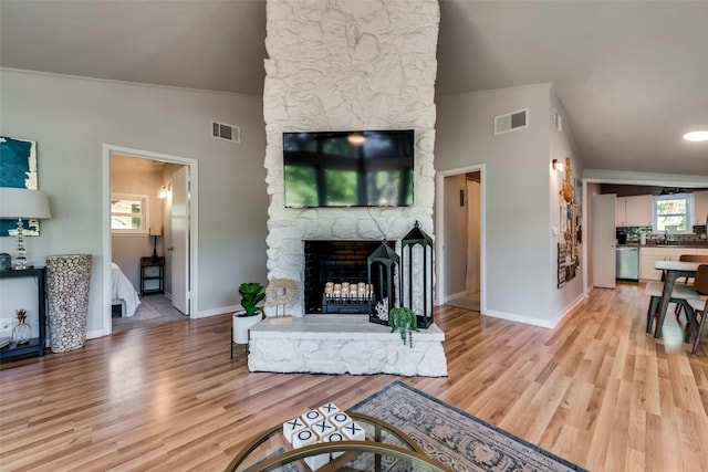 living room featuring a stone fireplace, light hardwood / wood-style floors, and lofted ceiling