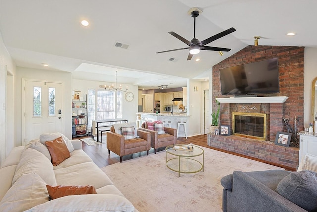 living room featuring ceiling fan with notable chandelier, lofted ceiling, light hardwood / wood-style flooring, and a brick fireplace