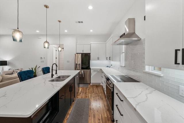 kitchen with a kitchen island with sink, sink, hanging light fixtures, wall chimney exhaust hood, and stainless steel appliances