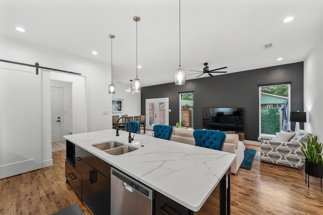 kitchen with dishwasher, sink, hanging light fixtures, a barn door, and an island with sink