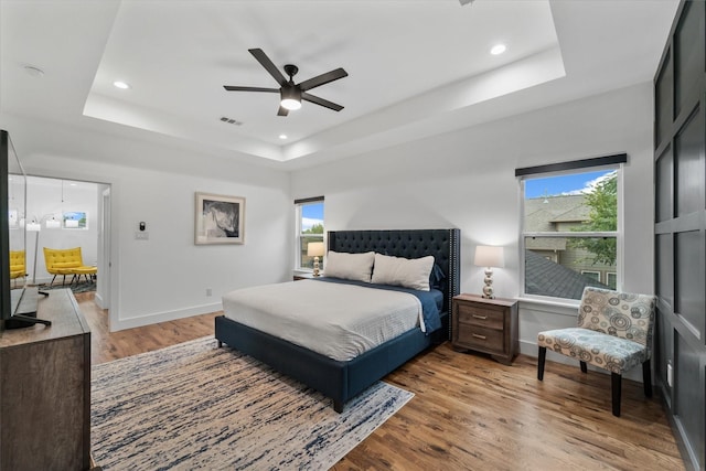 bedroom with hardwood / wood-style floors, a tray ceiling, and ceiling fan