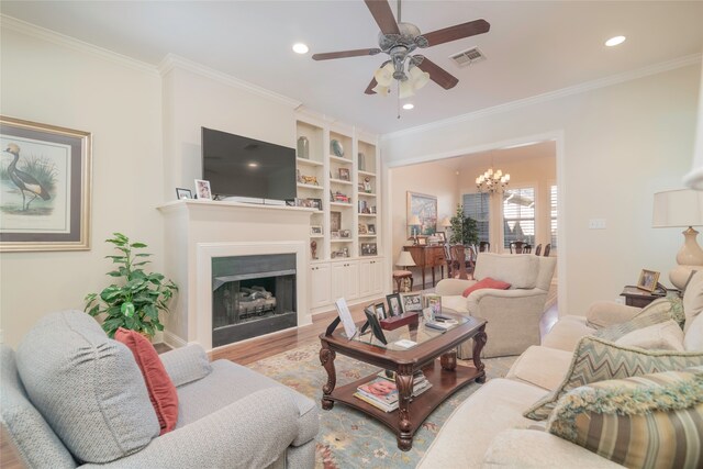 living room featuring ceiling fan with notable chandelier, built in features, ornamental molding, and light hardwood / wood-style flooring