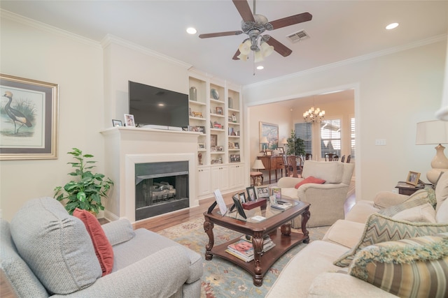 living room with ornamental molding, ceiling fan with notable chandelier, built in features, and light wood-type flooring