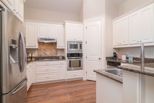 kitchen featuring appliances with stainless steel finishes, white cabinetry, dark hardwood / wood-style flooring, decorative backsplash, and dark stone counters