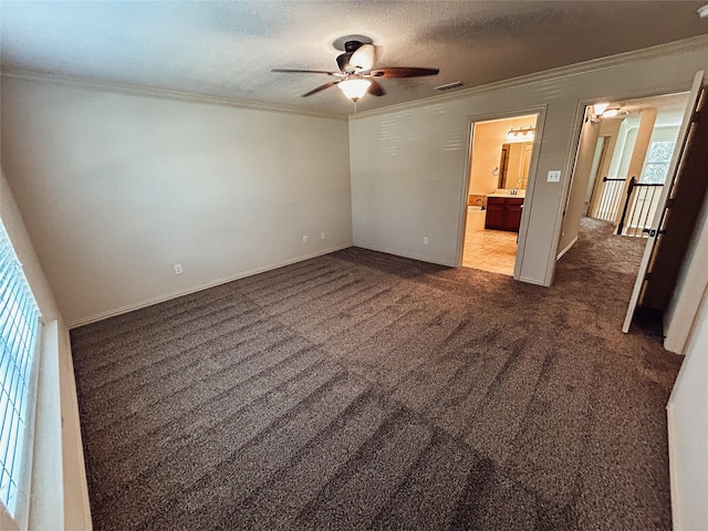 unfurnished bedroom with ensuite bathroom, crown molding, a textured ceiling, dark carpet, and ceiling fan