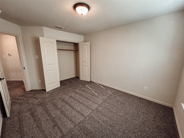 unfurnished bedroom with dark colored carpet, a textured ceiling, and a closet