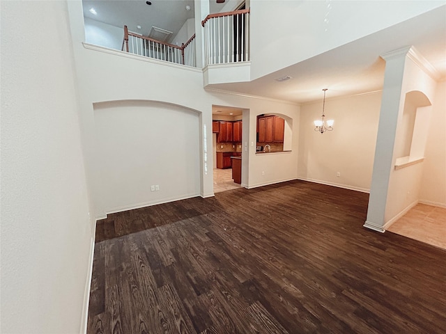 unfurnished living room with dark hardwood / wood-style flooring, a towering ceiling, crown molding, and a chandelier