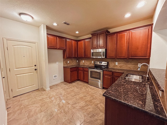 kitchen with sink, a textured ceiling, dark stone countertops, stainless steel appliances, and decorative backsplash