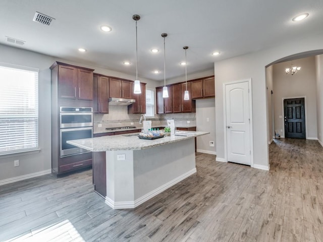 kitchen featuring a center island, stainless steel appliances, light stone counters, pendant lighting, and decorative backsplash