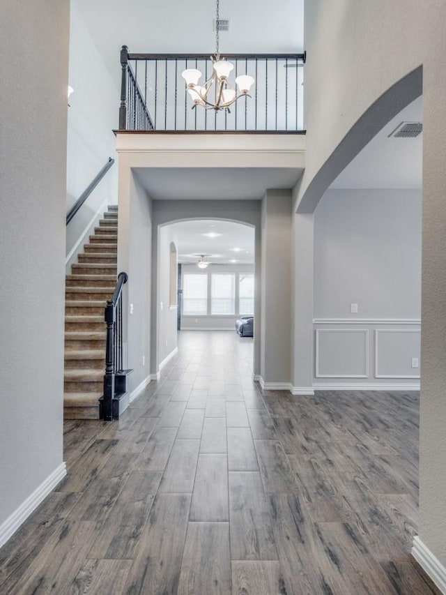 foyer entrance with a high ceiling, wood-type flooring, and ceiling fan with notable chandelier