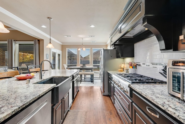 kitchen with sink, decorative light fixtures, dark brown cabinets, ornamental molding, and appliances with stainless steel finishes