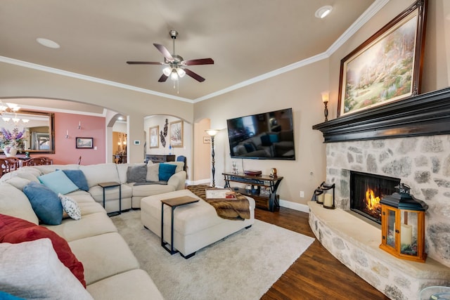 living room with ornamental molding, a stone fireplace, ceiling fan with notable chandelier, and light hardwood / wood-style flooring