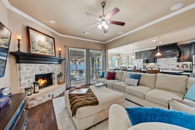 living room featuring crown molding, ceiling fan, a fireplace, and light hardwood / wood-style floors