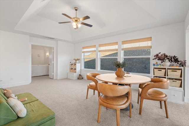 carpeted dining room featuring a raised ceiling, ceiling fan, and a healthy amount of sunlight