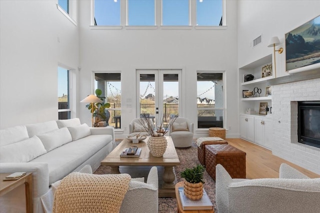 living room featuring built in features, a towering ceiling, light hardwood / wood-style floors, and a brick fireplace